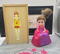 Wooden box with flat doll alongside Cupcake Surprise doll standing