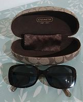 Sunglasses displayed with open Coach signature case and cloth