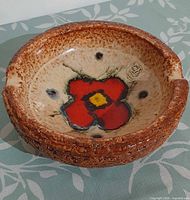 Top-down view showing full ashtray, poppy design, label, textured rim