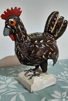 Three-quarter front view of carved and painted wooden rooster on base