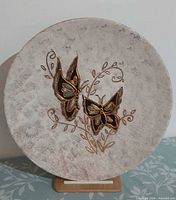 Front view of round pottery plate on stand showing full butterfly motif