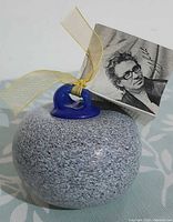 Front view of grey speckled glass curling rock ornament, blue handle, ribbon and artist photo tag visible