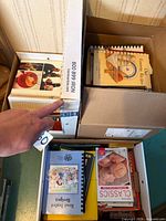 Top view of three boxes showing various cookbooks including a spiral-bound and binder