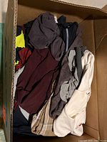 Box filled with assorted folded men’s clothes showing variety of garments