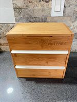Front view of bamboo storage cabinet showing hinged lid, two drawers with white pulls, doTERRA branding