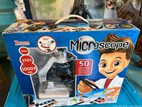 Front of box showing microscope image, magnification levels, accessories illustration