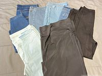 Pile of six pairs of jeans and pants in various colours laid out on bed