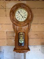 Full view of carved wood regulator wall clock hanging on wall
