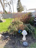 Lot showing two shepherd hooks, mosaic mushroom, flower stake, sun face stone in garden bed
