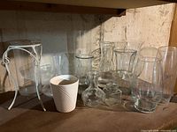 Shelf holding assorted clear glass vases, white planter, and metal stand