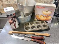 Full lot view showing two Bundt pans, aerator box, muffin tin, carving set, chip & dip bowl box