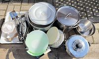 Overview of cookware, bowls, utensils and tray arranged outdoors