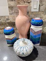 Group view of two striped canisters, pink vase, blue-speckled pumpkin dish
