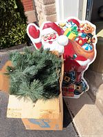 Cardboard box containing artificial tree branches beside vintage Santa sign