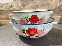 Two stacked enamel bowls showing exterior floral pattern and handles