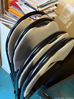 Stacked view of four beige padded folding chairs with black frames