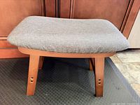 Side view of gray-cushioned wooden foot stool