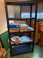 Full view of black plastic four-shelf utility rack with contents on shelves