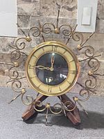 Front view of brass sunburst scroll wall clock on stand