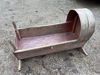 Side view of full wooden cradle showing hood, runners, finials, and red paint