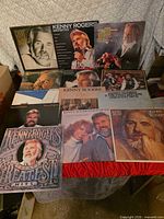 Overview of approximately 12 Kenny Rogers albums spread on table and propped at back
