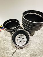 Stack of five large black plastic planters, one medium pot visible