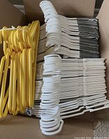 Box containing stacks of yellow, white, and gray-white plastic hangers