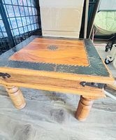 Overall view of solid wood coffee table showing square top, metal trim, turned legs