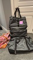 Two grey expandable GLOYUDA rolling bags stacked with pink striped tote