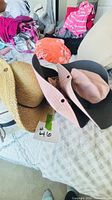 Straw hat, grey hat, pink hat stacked on bed