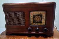 Front view showing wood cabinet, fabric grille, dial, and knobs