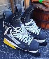 Full view of both Bauer Supreme skates standing upright with laces tied and yellow/white blade guards attached