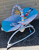 Side view of Disney Baby Mickey Mouse infant rocker showing blue seat, patterned trim, striped toy bar, metal frame