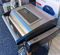 Closed grill showing stainless lid, viewing window, handle, indicator lights and temperature dial