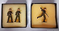 Two boxes open showing three painted metal toy soldier figurines positioned in yellow foam
