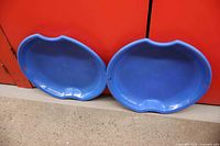 Two blue oval sleds side by side against cabinet