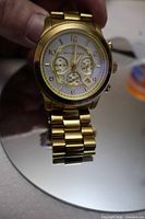 Front view of gold-tone Michael Kors chronograph watch showing dial, bracelet, and missing sub-dial hand