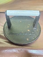 Top view of cast iron grill press showing handle and embossed logo