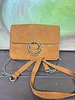 Front view showing faux-suede material, metal ring accent, chain strap