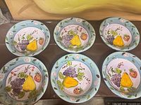 Six bowls laid out displaying interior fruit motif and blue rims