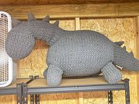 Full view of knitted grey dragon plush on shelf