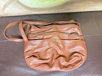 Front of brown leather crossbody showing front zip pocket, strap, overall shape