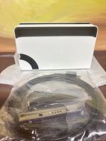 Front view of white Nintendo Switch OLED dock with bundled cables in plastic