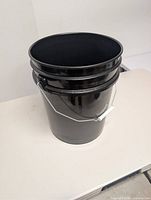 Angled view of black bucket showing open top and handle
