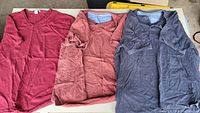 All three shirts laid out: burgundy V-neck, rust V-neck, charcoal Henley