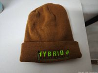 Front view of brown cuffed beanie showing embroidered HYBRID UTILITIES CO logo