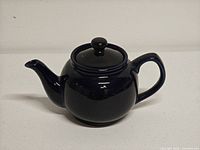 Side view of dark blue ceramic teapot with lid, showing spout and handle