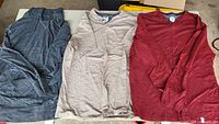 Three tops laid out: gray hoodie, beige henley, red long sleeve shirt