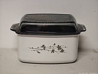Front view showing white enameled body, floral branch decal, black interior and glass lid
