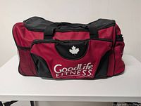 Front view of red and black GoodLife Fitness duffel bag showing logo and front pocket